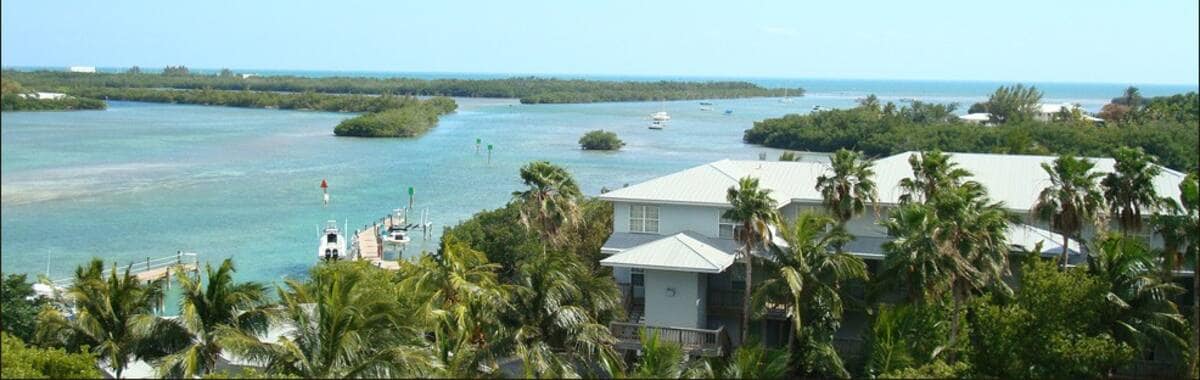 The image captures a panoramic view of the waterway between Key West and Stock Island, with lush greenery lining the shore. Boats can be seen gently navigating the calm waters, while the bright blue sky complements the tranquil scene.