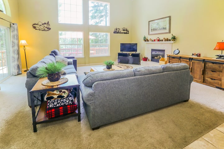 Pohľad na obývaciu izbu z jedálne.  TV, plynový krb, stropné ventilátory, všetko na diaľku.  Krásny výhľad vonku cez okná s celými stenami.  Stropy v tejto miestnosti sú vysoké asi 60 metrov s bielymi priečnymi trámami.