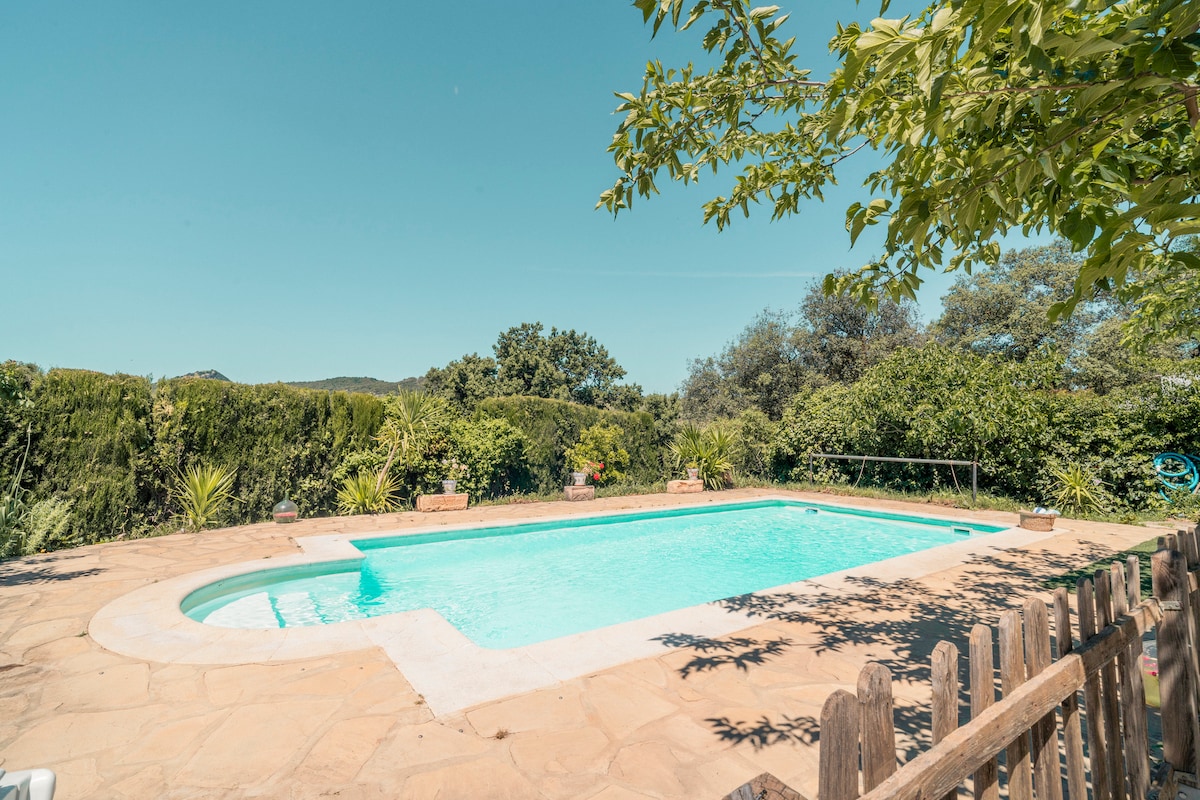 A private swimming pool is surrounded by lush greenery, creating a serene environment. The pool features a gentle blue hue and is set within a stone patio, offering ample space for relaxation. A wooden fence provides a boundary, enhancing privacy and natural views.