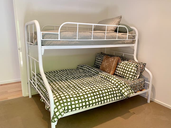 This bunk bed is single at the top and double on the bottom. The room has robes and a tall boy dresser with many drawers and a window looking out to garden.