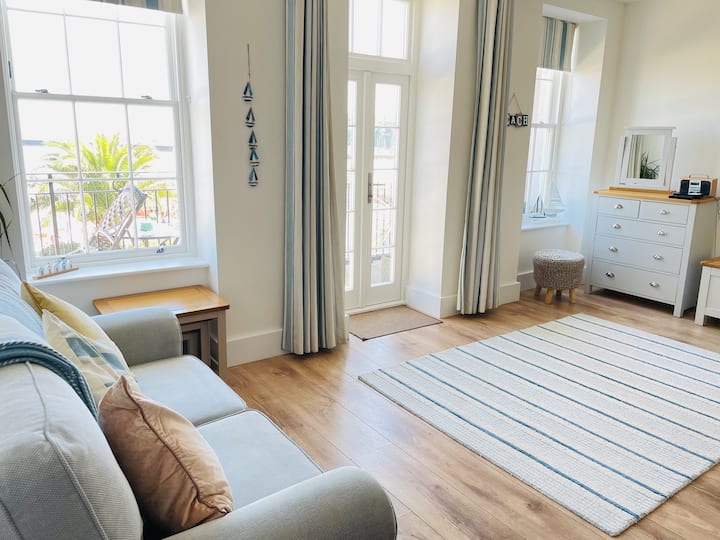 Sebule iliyo na kitanda cha sofa na milango ya baraza hadi kwenye roshani ya ufukweni iliyo na viti.