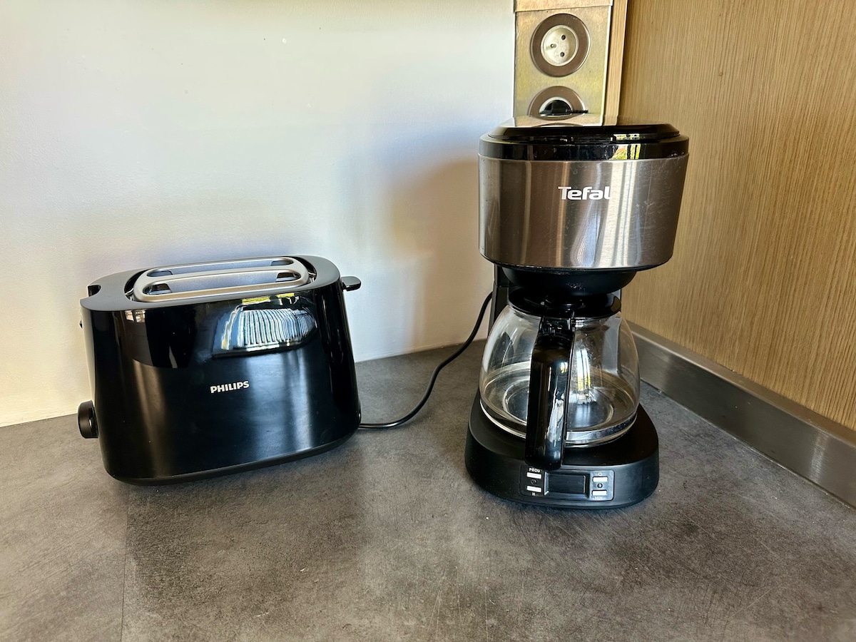 A sleek toaster and coffee maker are positioned on a modern countertop. The toaster is black with a chrome finish, while the coffee maker has a glass carafe and a black base, fitting seamlessly into the kitchen's contemporary design.