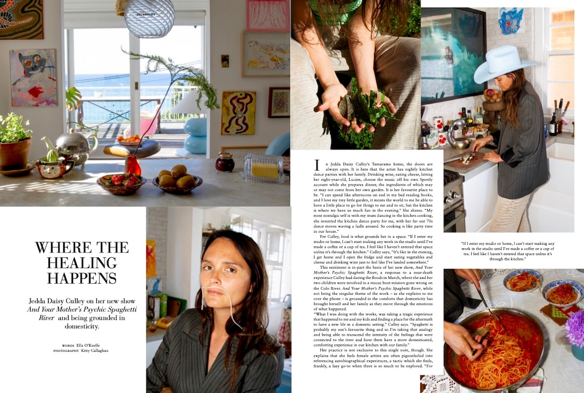 A bright kitchen with coastal views features a well-arranged countertop displaying fruits and decorative items. A person is seen cooking, with pots and fresh ingredients visible, emphasizing a welcoming culinary atmosphere. Sunlight enhances the serene environment through nearby windows.