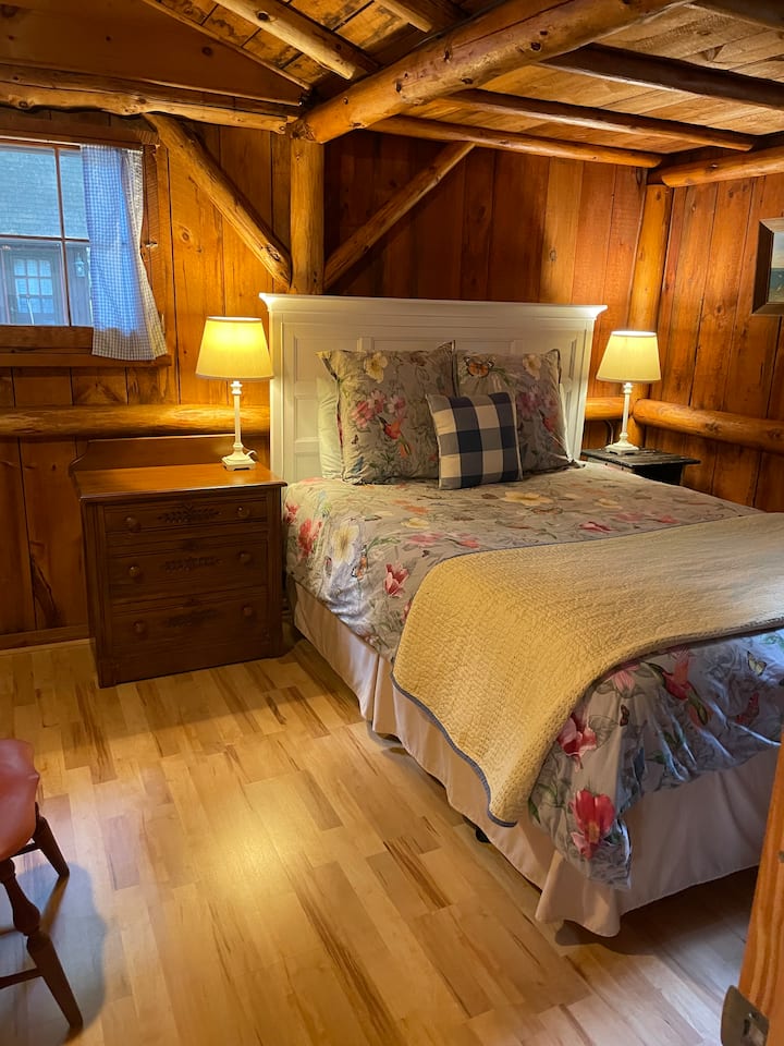 Segundo dormitorio con cama tamaño queen, cómoda y armario completo. A través de la ventana se ve un barracón separado. 