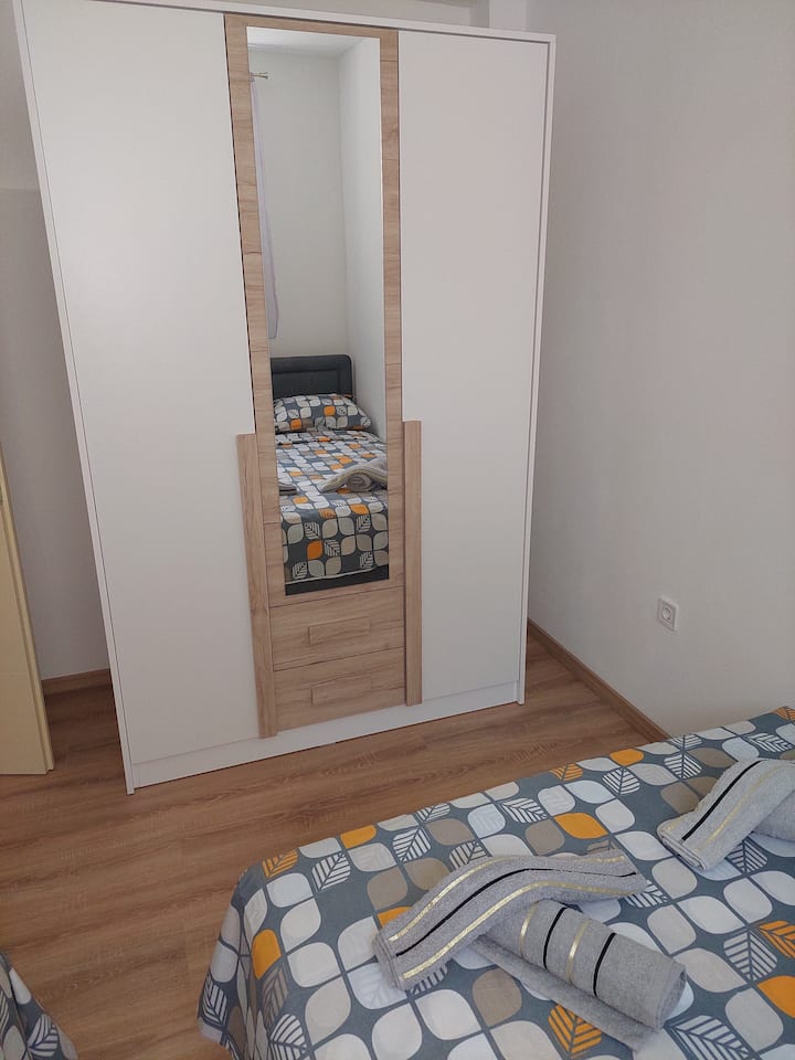 Room with a 140 cm bed and a 90 cm bed, a large wardrobe with a mirror and a bedside table.
The room is hospitable, with good insulation, double windows, mosquito protection, overlooking mandarins, kiwis, bananas, lavender and rosemary.