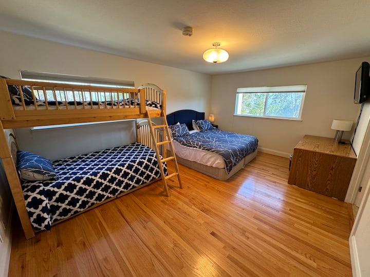 Dormitorio principal con cama California King y 2 camas individuales como litera de dos pisos, perfecto para familias o grupos. La habitación también incluye un escritorio y un televisor de pantalla plana montado en la pared para tu comodidad.