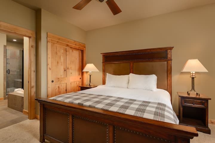 Bedroom 1 - Equipped with a plush king bed, closet for storage, a small seating area, flatscreen TV, an en-suite bathroom, and back patio access. 