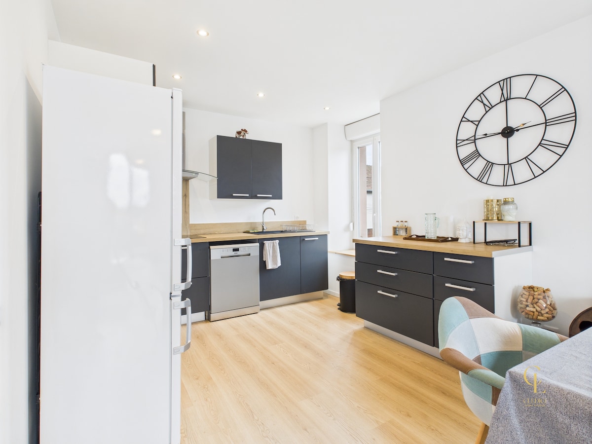 The image depicts a modern kitchen with a minimalist design. A spacious refrigerator stands against the wall, while sleek cabinetry provides ample storage. A stainless-steel dishwasher and sink are integrated into the countertop. A large clock adorns the wall, adding a functional element to the room.