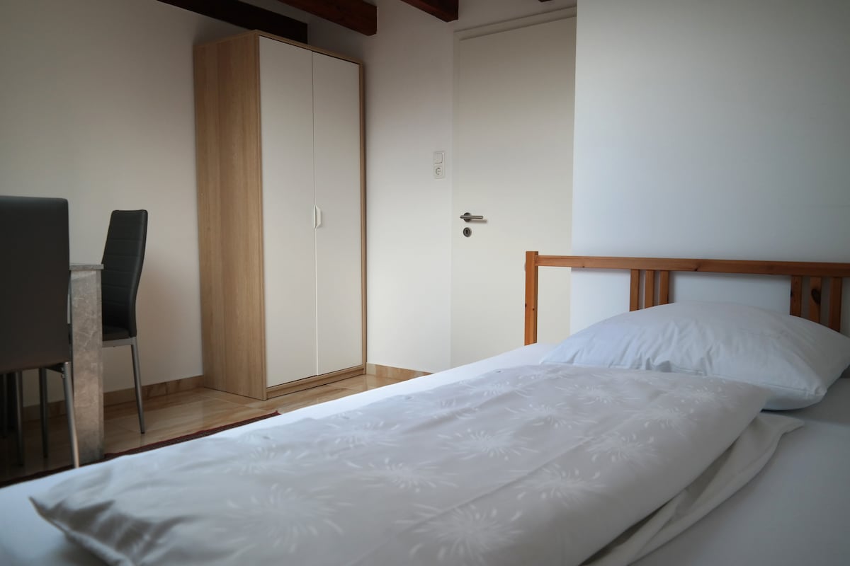 Spavaća soba s krevetom dimenzija 140 × 200 cm, ormarom i stolom s dvije stolice.