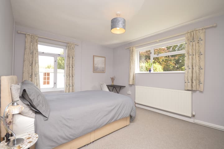 Master bedroom. Kingsized bed and a bank of inbuilt wardrobes.  Double aspect windows with garden views. Each bedroom features a desk table — perfect for mid-week work or remote working stays. Next to bathroom including full sized bath.