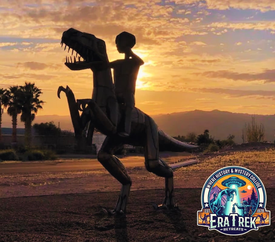 A sculptural representation of a dinosaur and a rider is highlighted against a sunset backdrop. The silhouette showcases the intricate metalwork, featuring the dinosaur in a dynamic pose with the rider on its back, surrounded by palm trees and mountains.