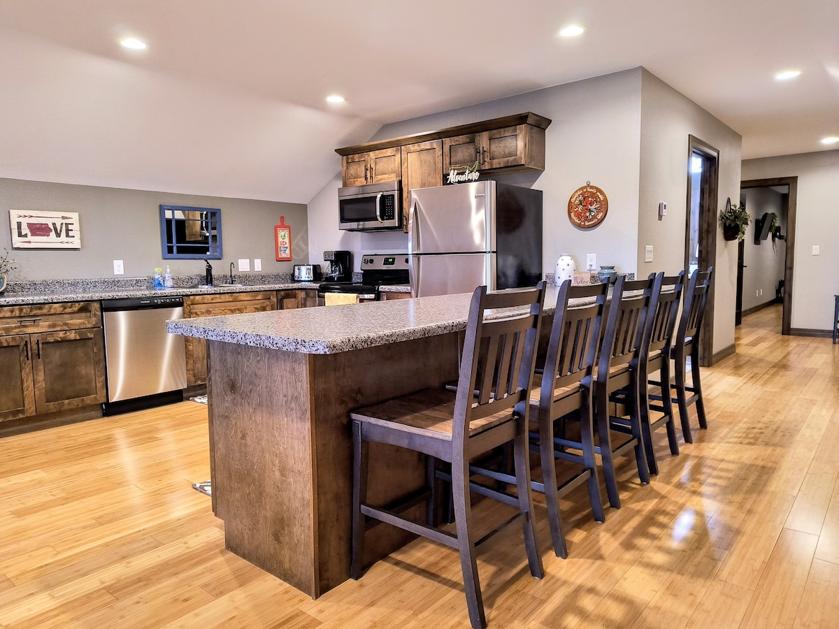 A spacious kitchen features modern appliances and ample cabinetry. A large island with seating for six is highlighted, providing a perfect gathering space. Sleek countertops complement the wood cabinets, and natural light illuminates the area through well-placed fixtures.