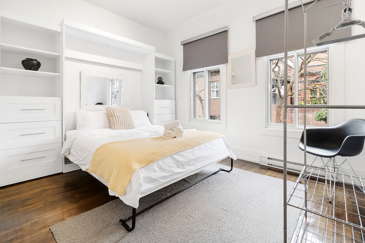 Dormitorio principal grande y luminoso con cama Queen. Mucha luz solar y espacio de almacenamiento. Hay un perchero y una silla adicional.