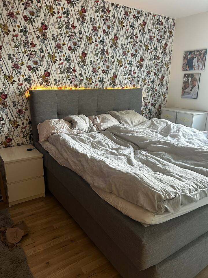 Chambre au rez-de-chaussée. Grand lit double. 180 cm. Fenêtre avec store roulant pour occultation. Éclairage chaleureux derrière le pignon.