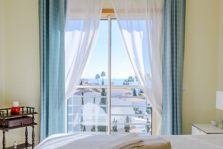 Réveillez-vous avec une vue sur la mer et la verdure à travers la fenêtre de votre chambre, où les rideaux transparents ajoutent une sensation de lumière confortable.