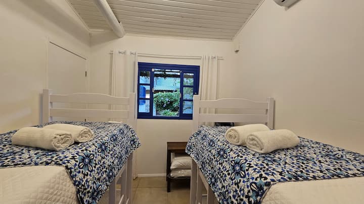 Chambre partagée avec lits superposés, draps en percale blanche 200 fils, couette, serviettes de bain Buddemeyer, chauffage électrique (en hiver), banc à bagages, ventilateur, climatisation split inverter (refroidissement) et vue sur la pergola.