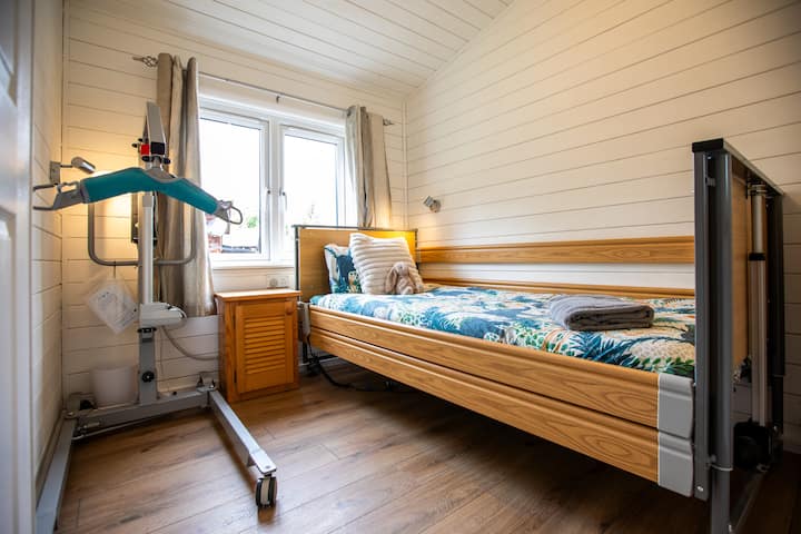 ห้องนอนที่เข้าถึงได้มีเตียงปรับความสูงได้และเครื่องพยุงตัวแบบเคลื่อนที่ เหมาะสำหรับผู้เข้าพักที่เคลื่อนไหวได้จำกัด สะดวกสบาย สว่าง และมีสิ่งอำนวยความสะดวกครบครันเพื่อการเข้าพักที่ปลอดภัยและผ่อนคลาย การใช้เครื่องยกต้องใช้สลิงของคุณเอง