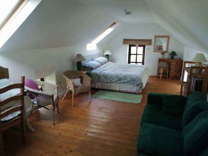 Upstairs - Double bed with little door leading out to the timber balcony. The forest-green sofa in the foreground folds out to a double bed. Velux windows give great light and views of mature beech trees and starry skies, and have pull-down shades.