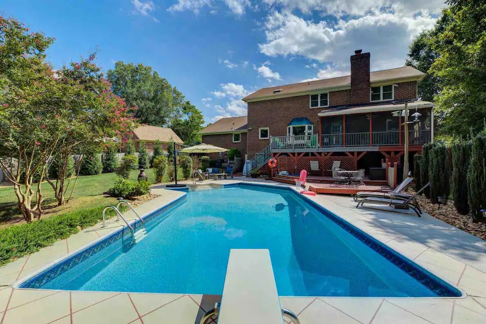 The outdoor space features a heated pool surrounded by a well-maintained yard. Comfortable lounge chairs are positioned nearby, and a deck extends from the house. Lush greenery and decorative trees create a serene environment, inviting outdoor relaxation and enjoyment.