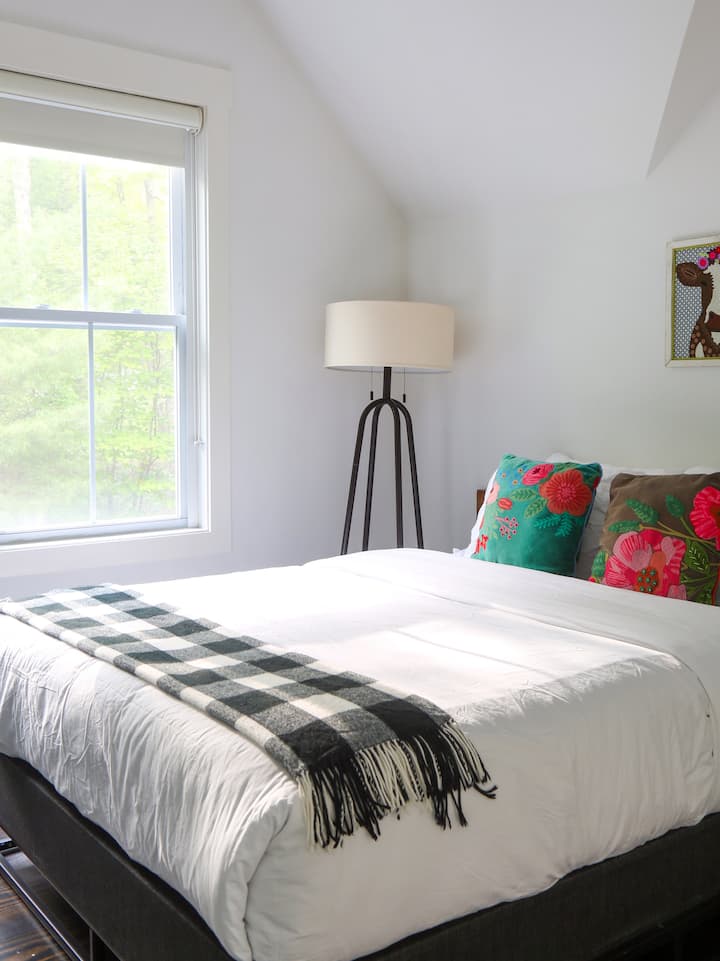 Soft bedding, fresh light, and floral pillows bring charm and coziness to this upstairs bedroom—perfect for a restful night after a day outdoors.