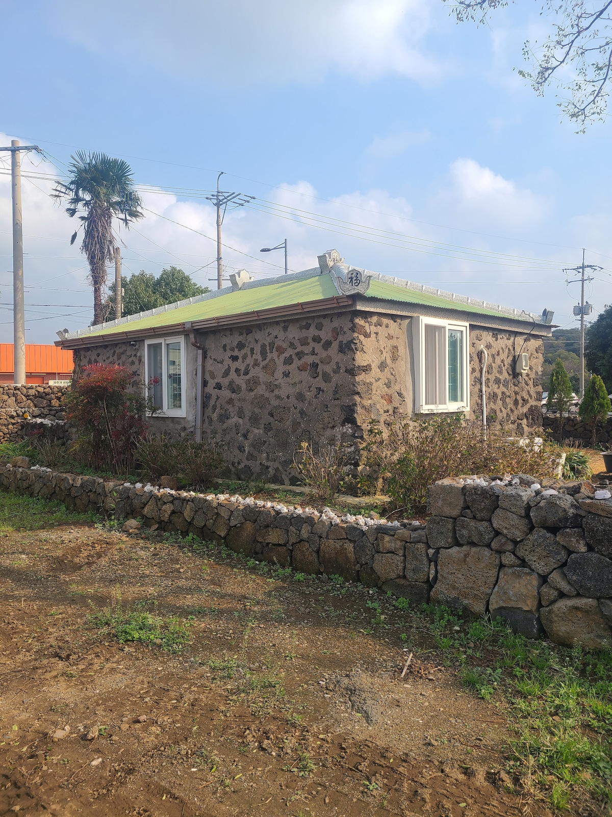 A stone house, featuring a traditional design, is set against a clear sky. Large windows allow natural light to fill the room. A grassy area surrounds the home, bordered by a low stone wall that enhances the rustic charm.
