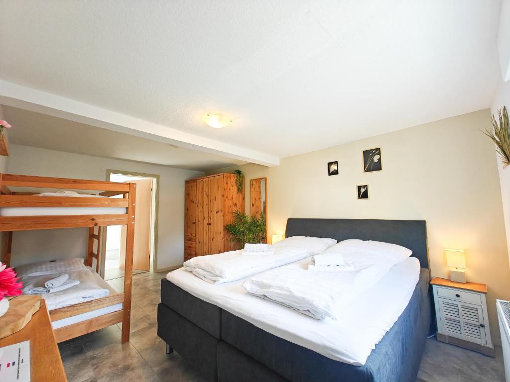 A comfortable guest room features a spacious bed with crisp white linens and a bunk bed in the corner. Wooden wardrobes and bedside lamps provide functional decor. Soft, neutral tones create a calming space, with natural light illuminating the room.