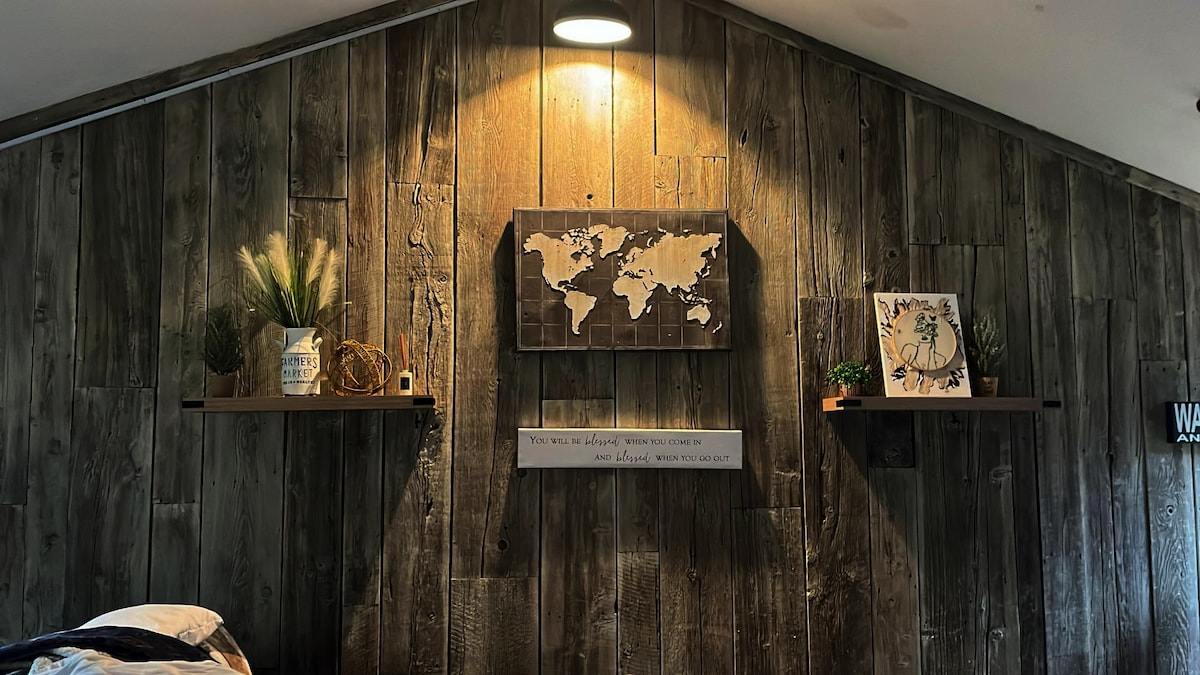 A rustic wooden wall features two shelves adorned with decorative items. A world map is displayed on the center of the wall, complemented by a clock and a plant on the shelves. Soft lighting highlights the textures of the wood.