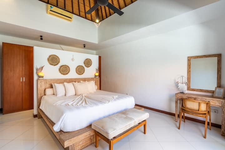 The master bedroom at Villa Jiwa offers a luxurious king-size bed, a stylish ensuite bathroom with a bathtub, a dressing table, and serene views of the sparkling pool.