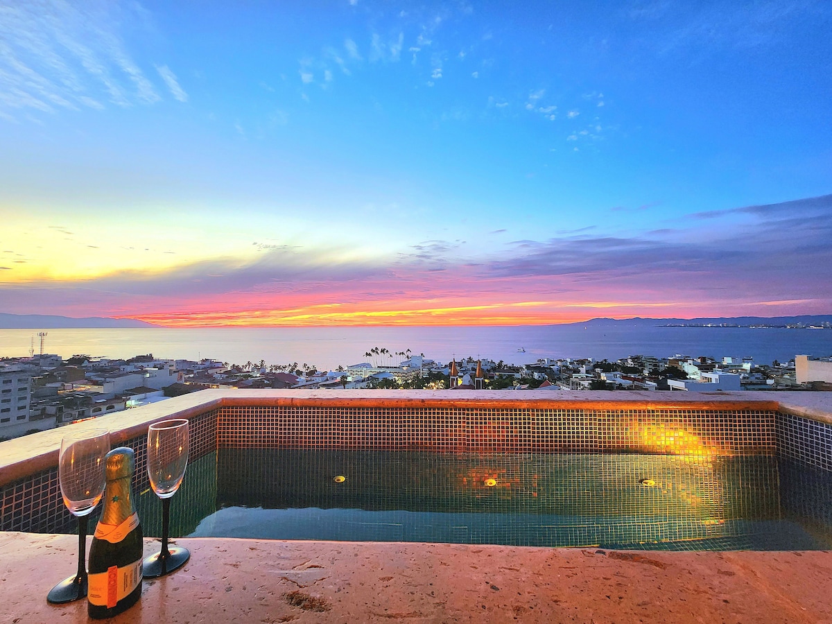 A private pool reflects the vibrant colors of the sunset over the ocean. Champagne glasses are positioned nearby, inviting relaxation. The panoramic view showcases the tranquil water and surrounding landscape, highlighting the serene ambiance of the space.