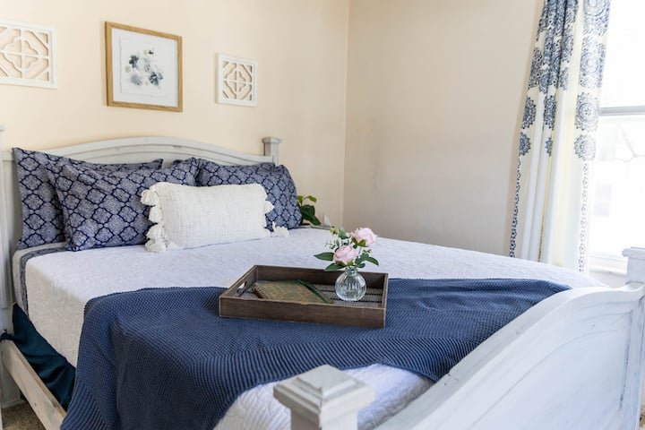 Cama tamaño queen con sábanas de algodón. 2 almohadas de espuma viscoelástica y 2 almohadas alternativas de plumas. También hay una mesita de noche con una lámpara y una máquina de sonido.