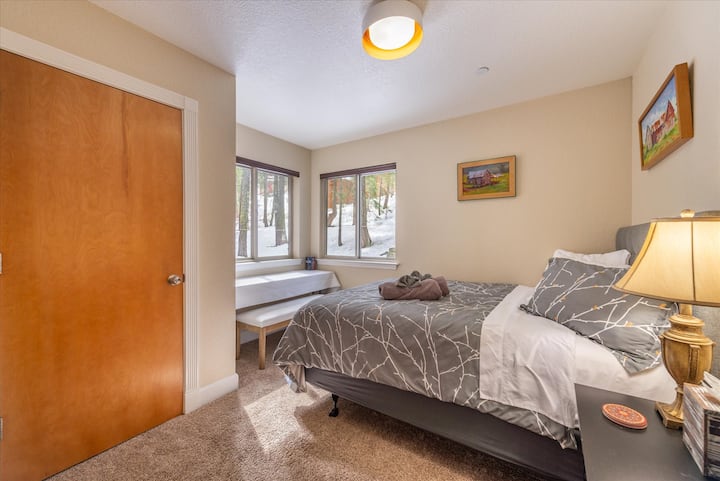 Cette chambre, la chambre 1 sur trois chambres au total, dispose d'un lit Queen Size, d'un placard, d'une petite commode de chevet, d'une vue sur la forêt derrière la maison. Il dispose d'une longue table et d'un banc rembourré à hauteur de table, offrant un espace de travail privé ou un espace de lecture.