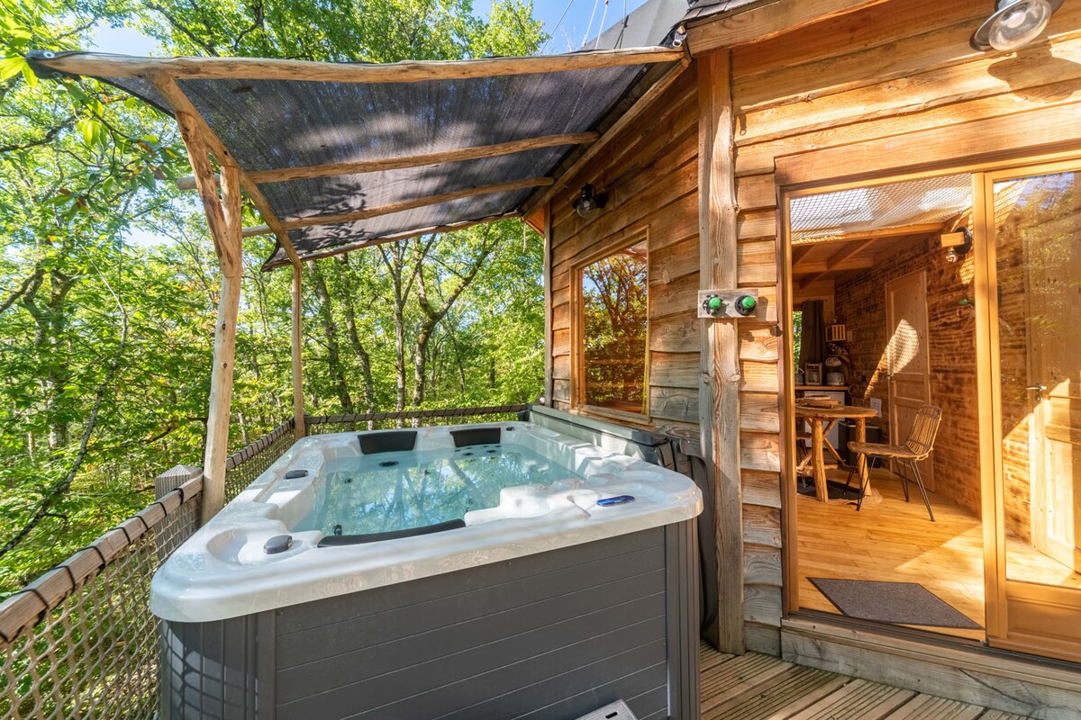 A private spa is nestled on a wooden deck, surrounded by lush greenery. The spa is well-maintained, featuring jets and a spacious interior. Adjacent to the spa, large glass doors provide access to an inviting interior space, blending seamlessly with the outdoor environment.