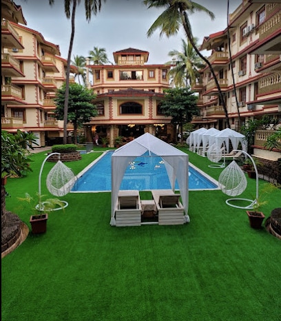 A well-maintained outdoor area features a large swimming pool surrounded by lush green grass. Stylish shade structures are placed near the pool, and tropical plants add to the serene environment. The surrounding buildings showcase a traditional architectural style, enhancing the overall ambiance.