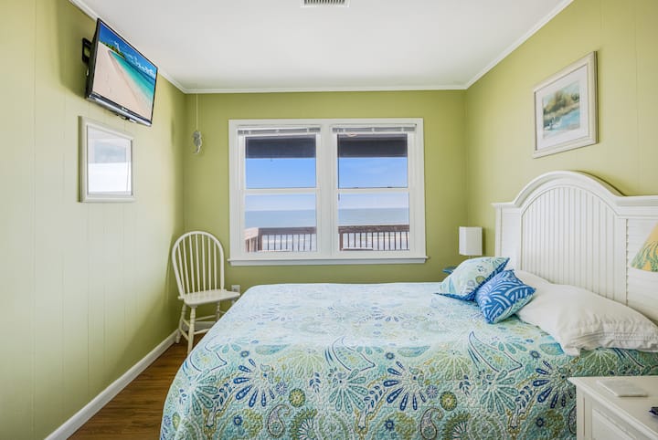 غرفة بحجم كوين بإطلالة على المحيط وخزانة ملابس مدمجة مع مرآة وخزانة ومروحة سقف وتلفزيون بشاشة مسطحة مثبت على الحائط.