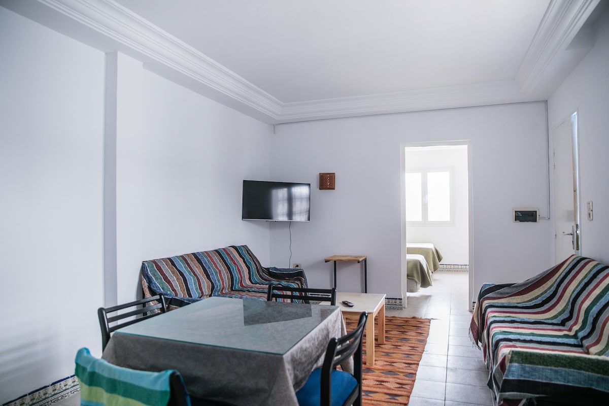 Lichte woonkamer met airconditioning, bank, salontafel en tv.