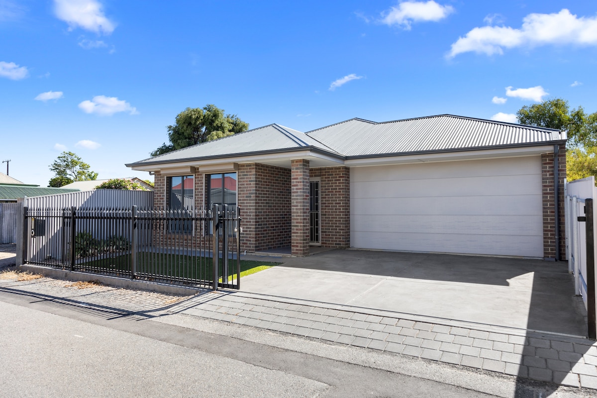 A modern brick home is showcased with a sleek design and a well-maintained exterior. The property features a double garage and a secured front fence, offering privacy. A neatly paved driveway leads to the entrance, while a small grassed area adds a touch of greenery.