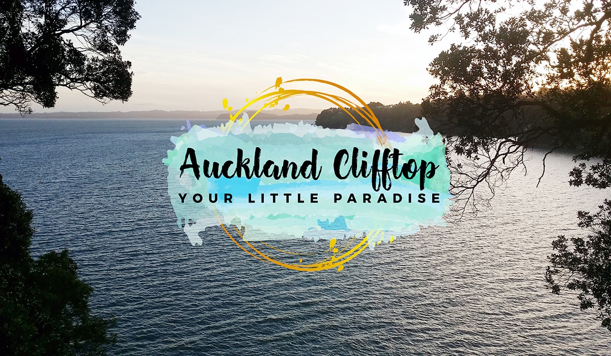 A serene view of a body of water is displayed, framed by lush trees along the shoreline. The sunset casts a soft, warm glow across the scene, inviting peaceful reflection. Text overlay reads 'Auckland Clifftop Your Little Paradise,' enhancing the tranquil atmosphere.