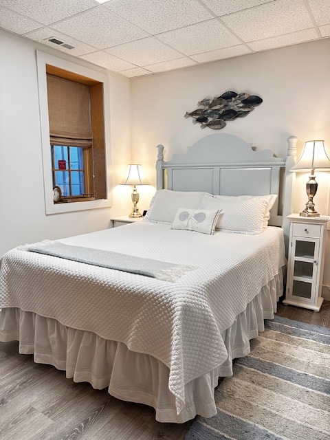 A serene sleeping area features a queen-size bed dressed in white linens, complemented by a soft quilt. Two bedside lamps provide gentle illumination, while a decorative fish artwork adorns the wall above the headboard. A subtle rug adds texture to the clean, modern space.