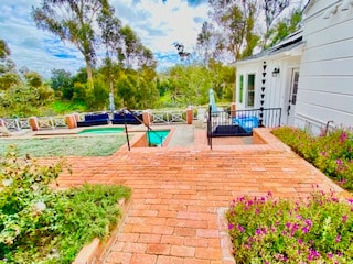 A brick pathway leads towards a private outdoor area, surrounded by lush greenery and colorful flowers. The saltwater pool is visible in the background, along with comfortable seating options and a patio area. The view overlooks a serene canyon landscape.