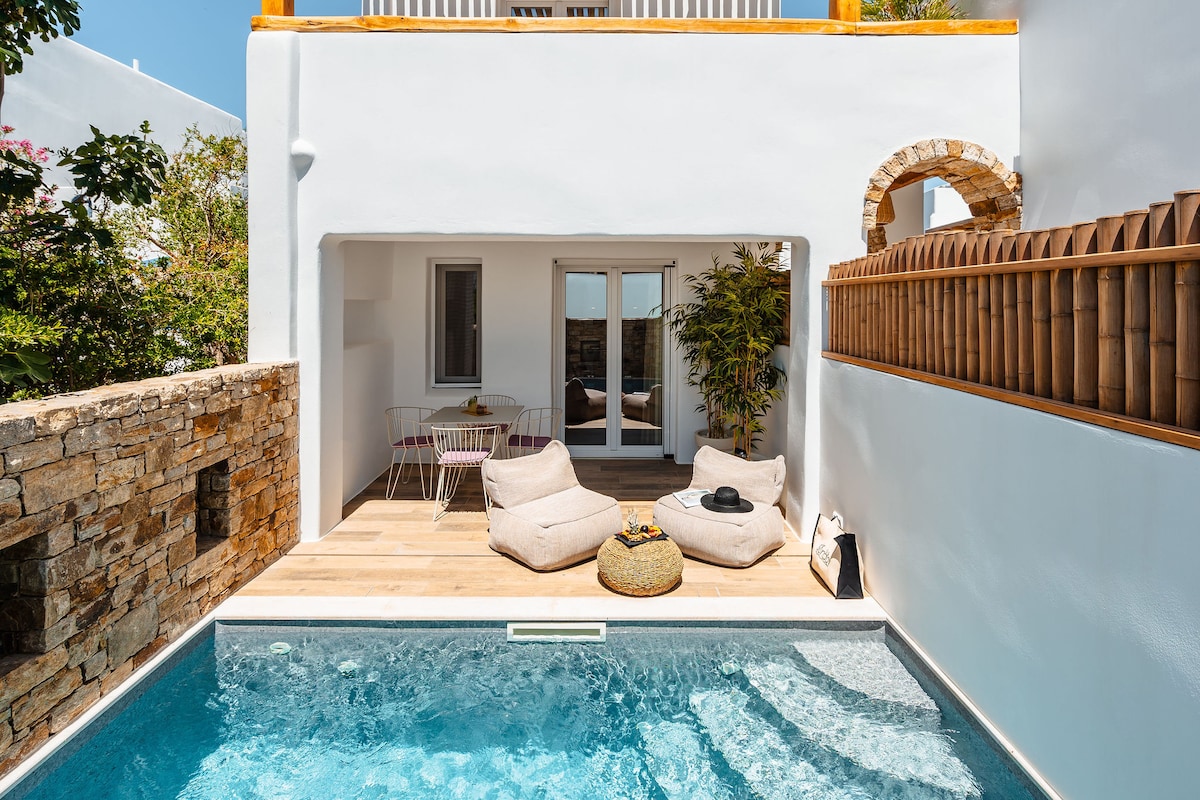 A private outdoor area features a heated plunge pool, bordered by wooden decking. Two large bean bags provide comfortable seating, with a small round table and chairs positioned nearby. Lush greenery grows along the walls, enhancing the tranquil atmosphere.