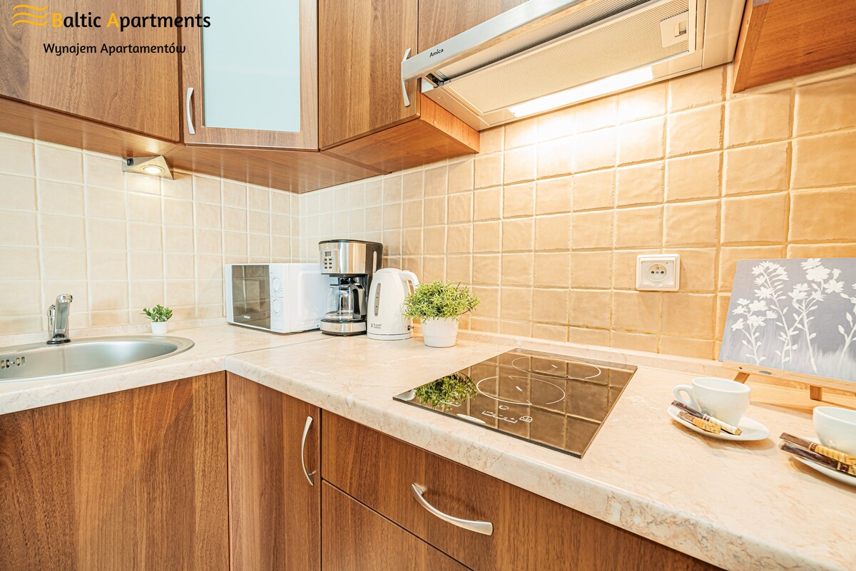 A fully equipped kitchen features wooden cabinetry, a countertop with an electric cooktop, and essential appliances including a microwave, coffee maker, and kettle. Dishes and utensils are neatly arranged beside a small decorative element on the counter, enhancing the functionality of the space.