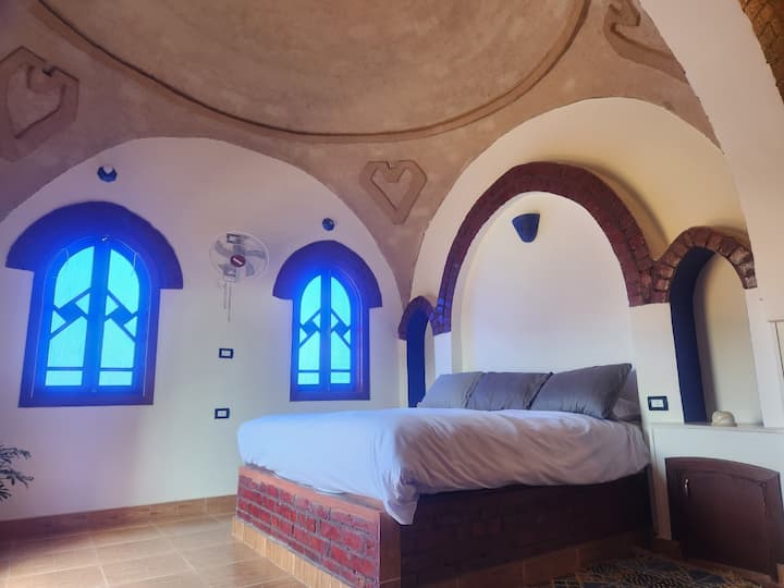 Cama tamaño king en una habitación grande con balcón, tocador, 2 armarios para colgar ropa y 2 con estantes.  Techo abovedado con corazones y la geometría del círculo.