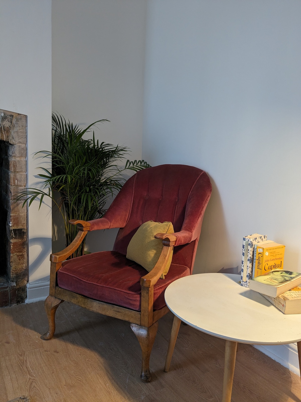 A comfortable, vintage armchair with rich burgundy upholstery is positioned next to a small, round table. A decorative green cushion rests on the chair. A potted plant adds a touch of greenery to the warm, inviting corner.