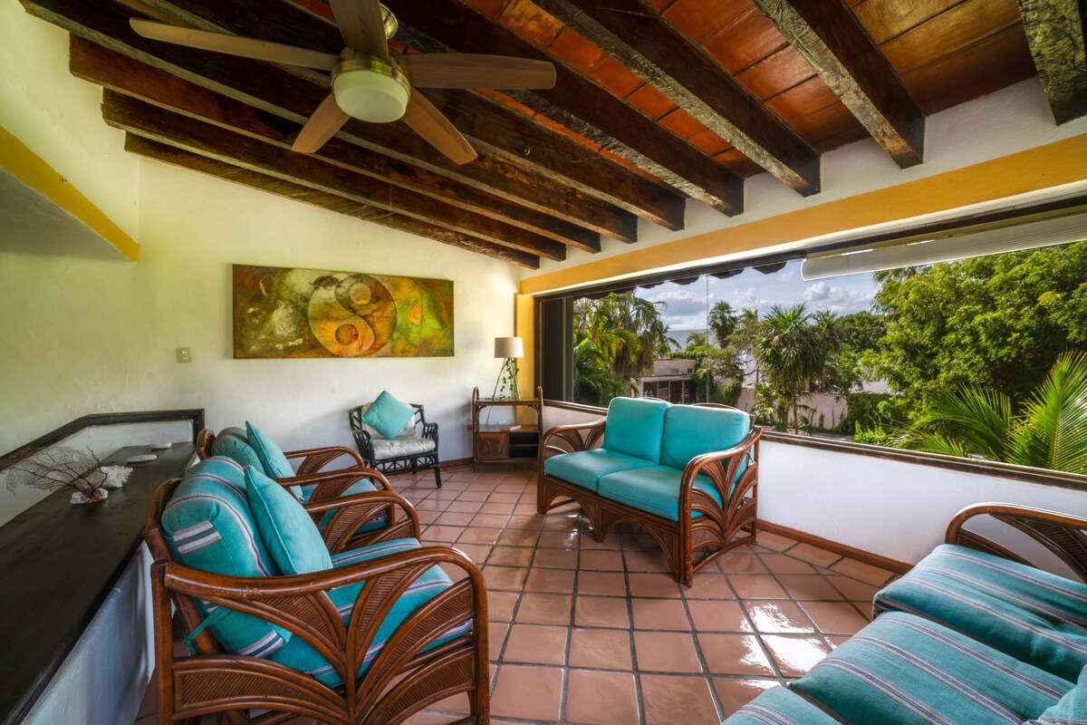 Espaciosa y luminosa estancia de estar con una bella vista a los jardines y palmeras, techada con vigas de madera que dan un especial sabor al descansar. Cuenta con ventilador de techo y un amplio vetanal lateral.