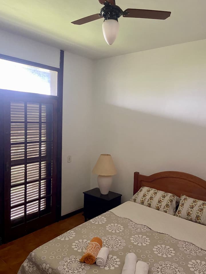 Chambre avec lit double avec ventilateur de plafond et télévision. Accès au balcon principal, relié à deux autres chambres et au salon, donnant sur l'entrée de la maison. Armoires disponibles.