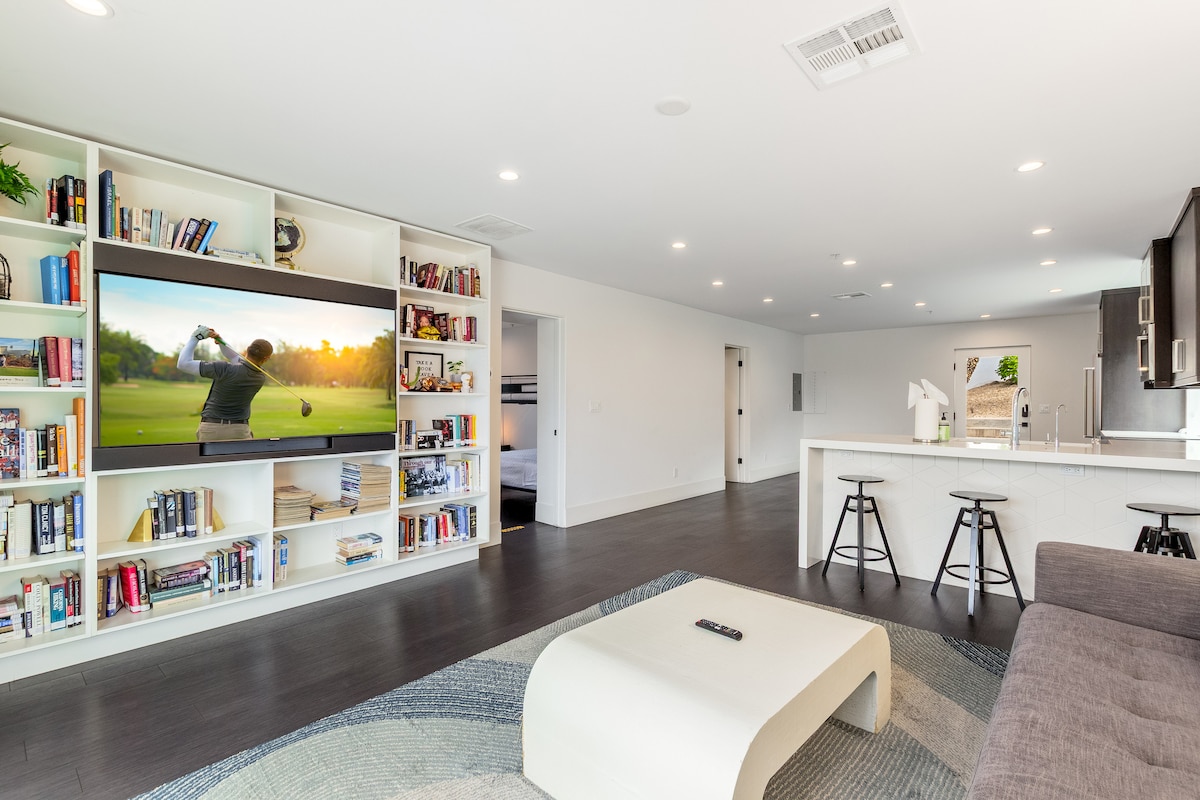 Relax and unwind in this chic lounge, featuring built-in shelving, a sleek bar, and a large-screen TV for ultimate comfort.