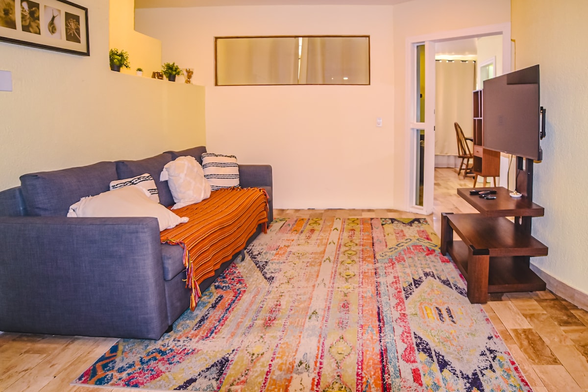 მყუდრო, ღია გეგმარების მისაღები ოთახი, რომელშიც არის კომფორტული დივანი და ბევრი ბუნებრივი სინათლე. თბილი, პრაქტიკული სივრცე დასასვენებლად, ყავის დასალევად ან ქალაქში დღის გეგმის შესადგენად, მარტო თუ კომპანიაში.