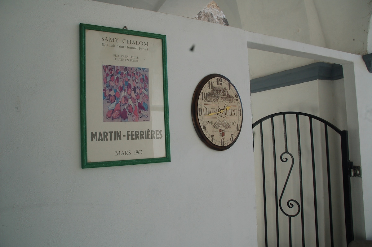 A wall is decorated with a framed vintage poster depicting colorful figures and a round clock, indicating the time. The white wall creates a clean backdrop, enhancing the visual appeal of the framed artwork and clock.