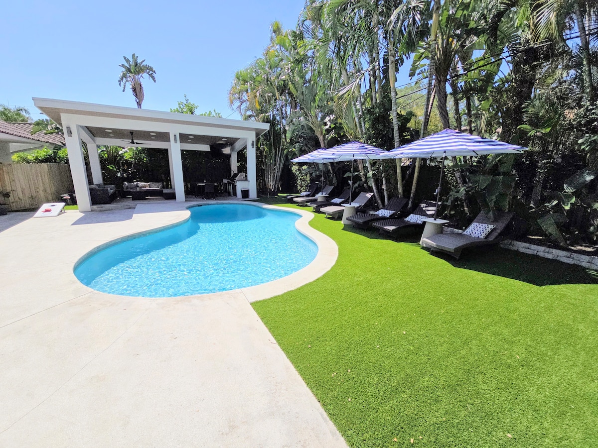 A heated saltwater pool is surrounded by well-maintained tropical landscaping. Shaded lounge chairs are positioned near the pool, offering comfort and relaxation. An open gazebo is visible in the background, providing an inviting space for gatherings and leisure activities.