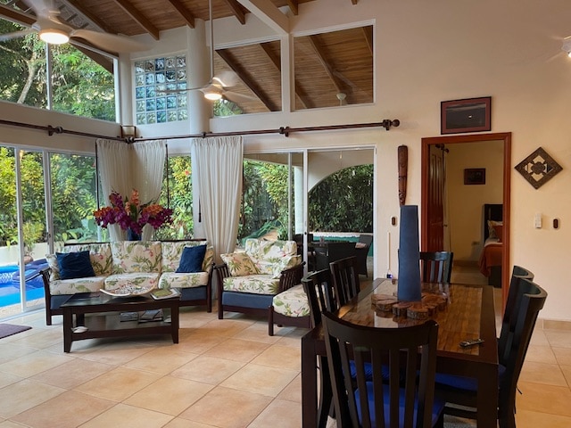 A spacious living area is characterized by large glass doors that overlook vibrant greenery, allowing natural light to flood the room. Comfortable seating is arranged around a wooden coffee table, complemented by a dining area with a dark wood table and chairs.